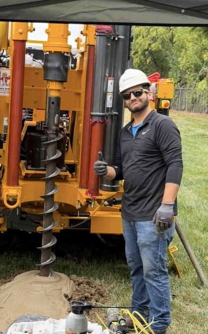 Jon White wearing a hard hat beside drilling equipment